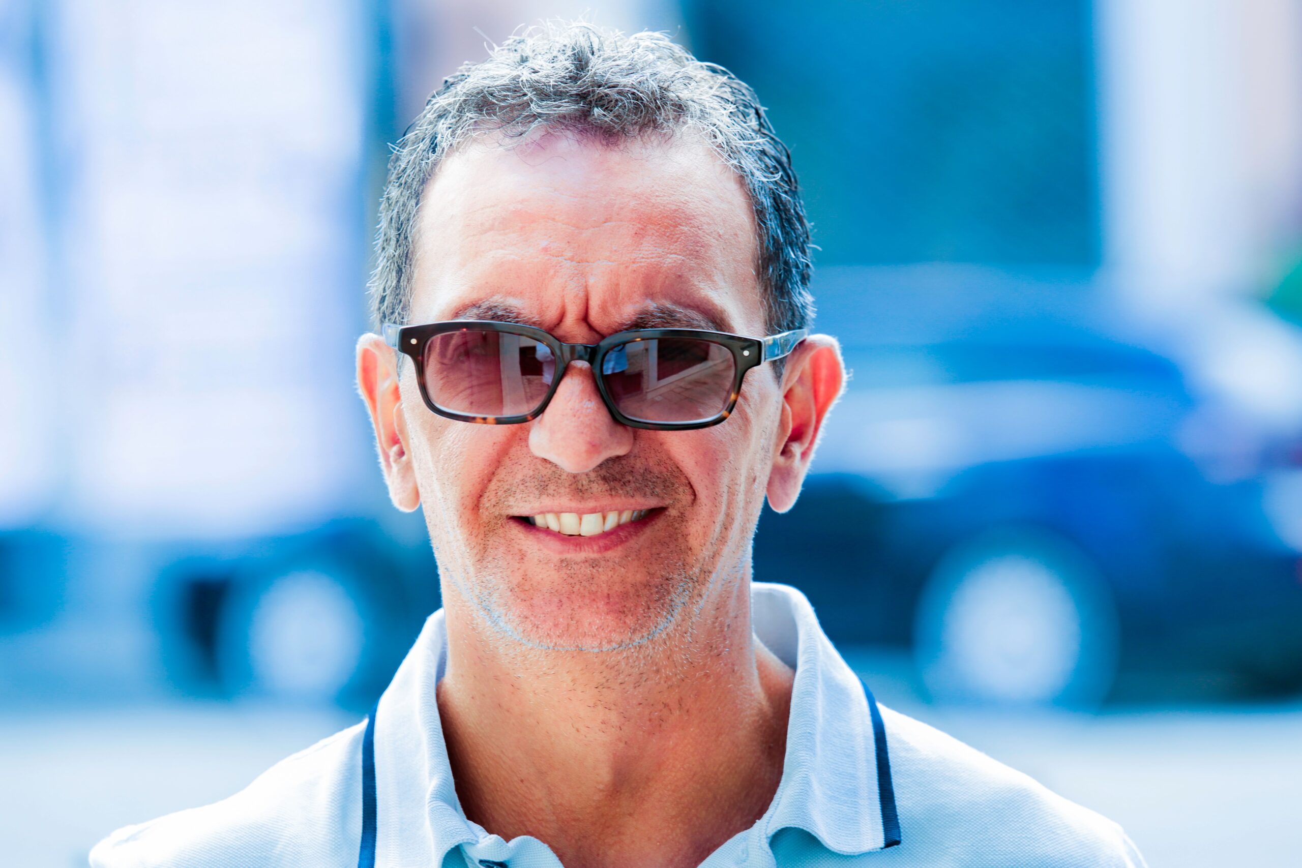 Portrait of a cheerful middle-aged man wearing sunglasses, captured outdoors with a soft focus background.